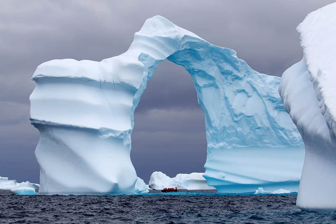Huge Arch Shaped Iceberg in Antarctic waters with a boat in the distance