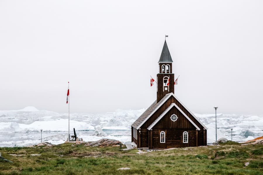 Exterior view of the old wooden Zion's Church with icebergs in the background