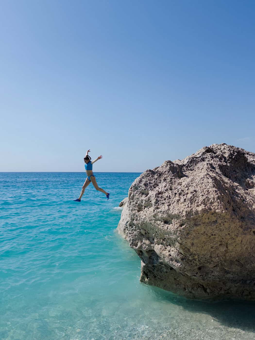 Girl jumping off the rocks at Kavalikefta beach in Lefkada, Greece