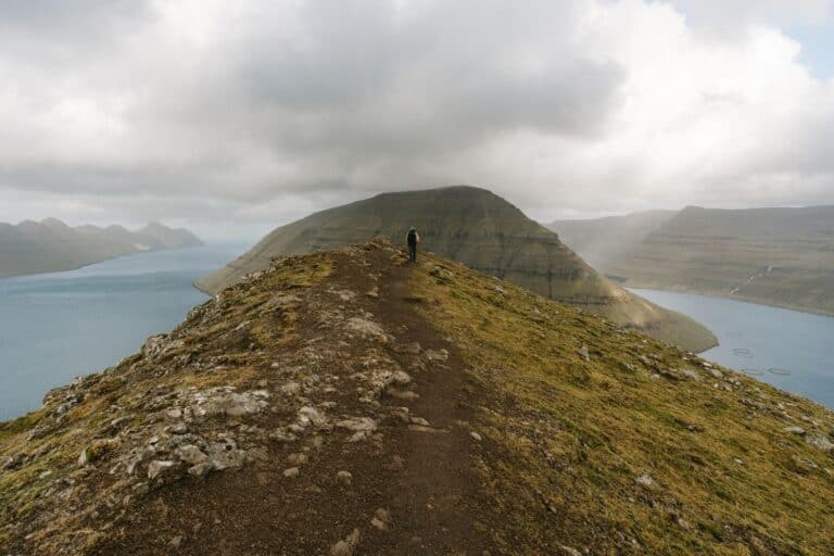 Hiker standing at the top of Klakkur with dramatic mountain and fjord views in the Faroe Islands.