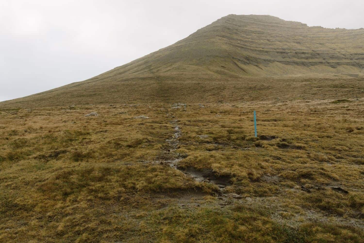 Muddy grass hiking trail climbing the mountain above Viðareiði in the Faroe Islands